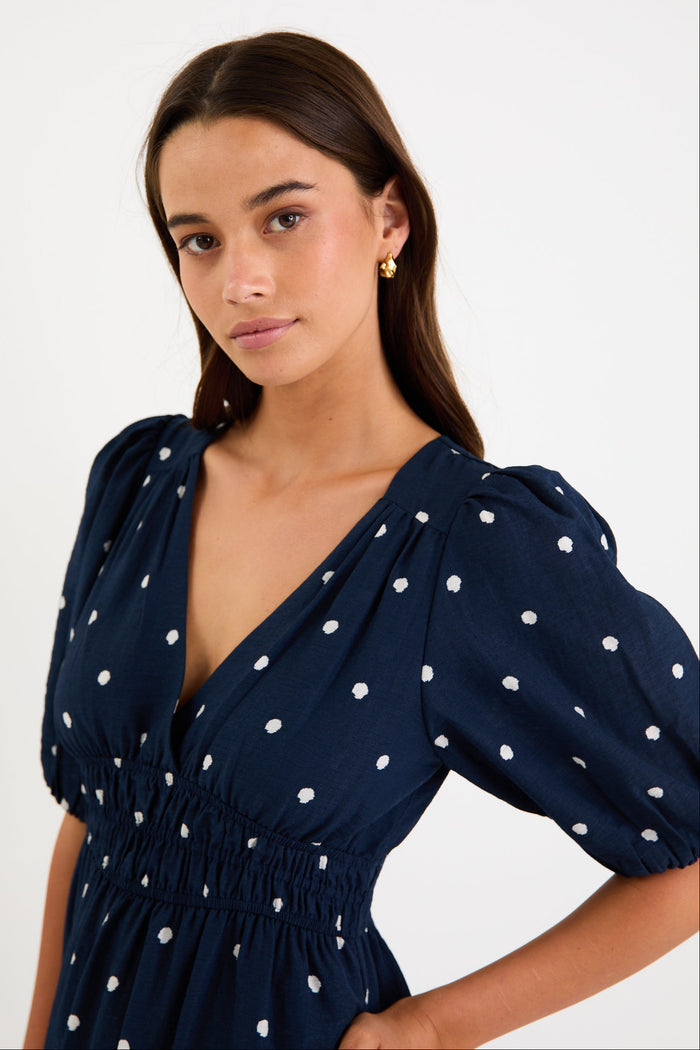 Model wearing a navy polka dot maxi dress with a V neckline, flutter sleeves and an elasticated waist