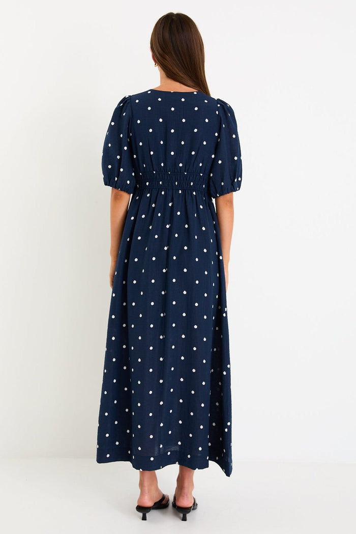 Model wearing a navy polka dot maxi dress with a V neckline, flutter sleeves and an elasticated waist