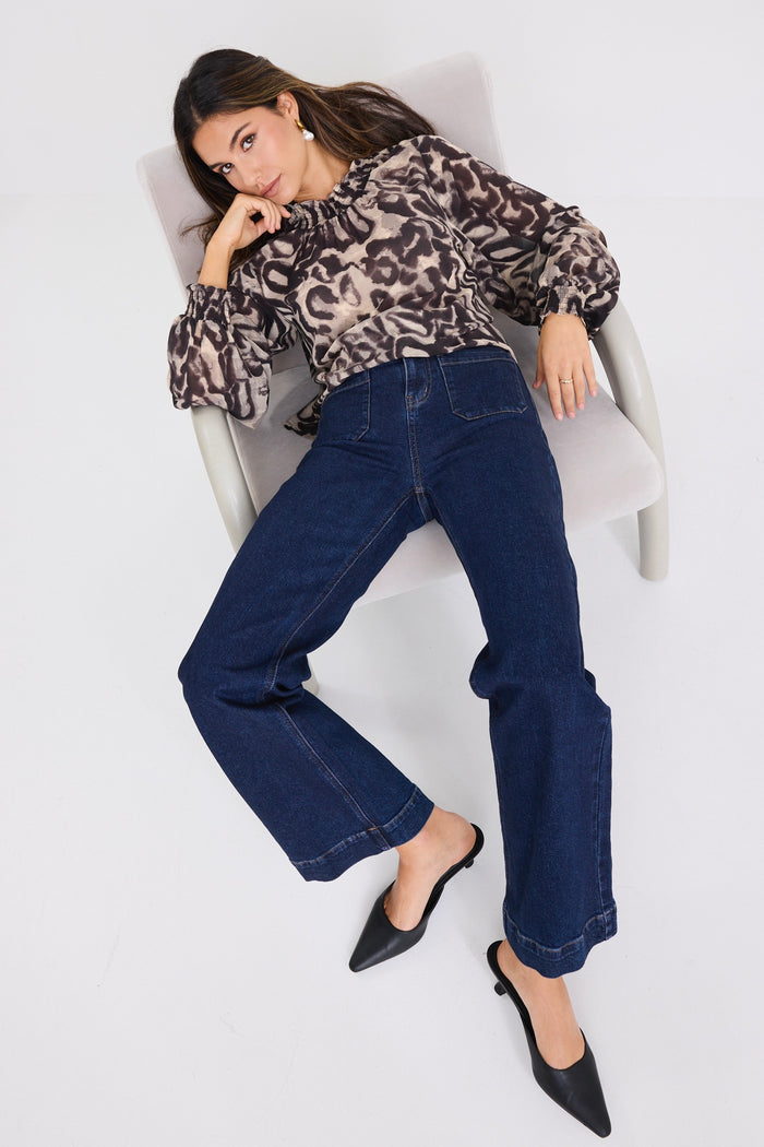 Woman wearing a charcoal animal print long-sleeve blouse with shirred neckline and cuffs, paired with dark high-waisted jeans.
