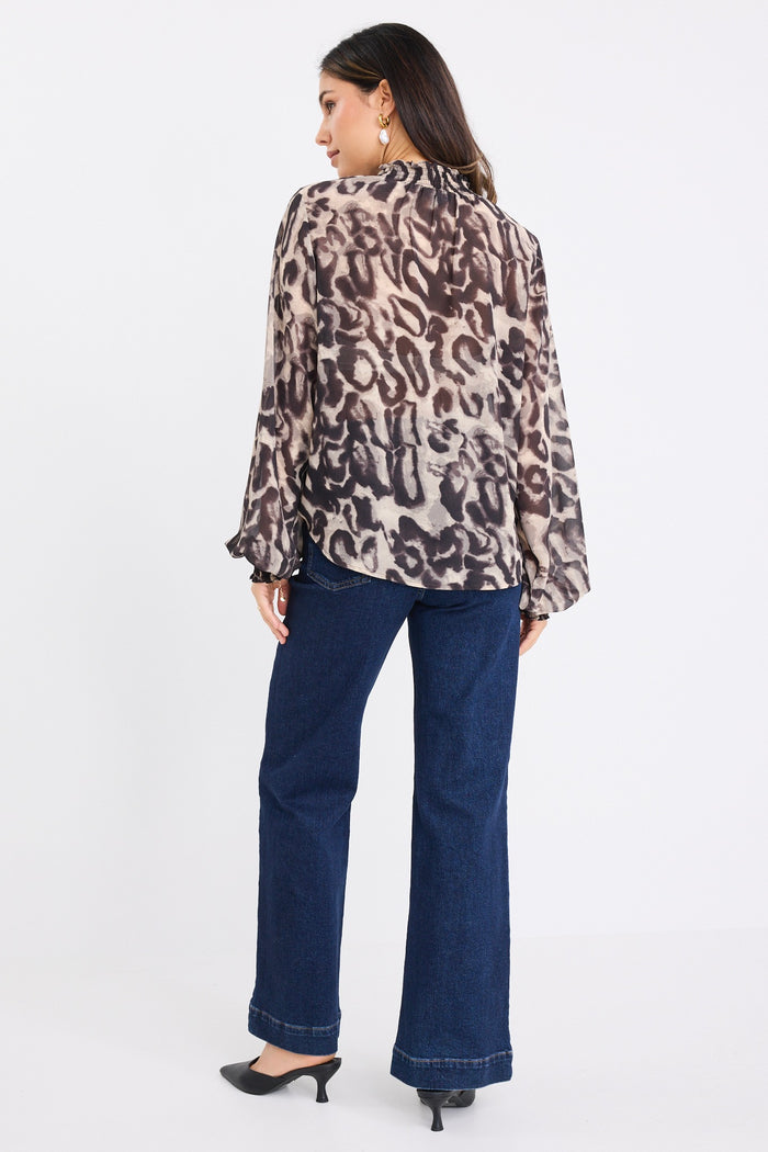 Woman wearing a charcoal animal print long-sleeve blouse with shirred neckline and cuffs, paired with dark high-waisted jeans.
