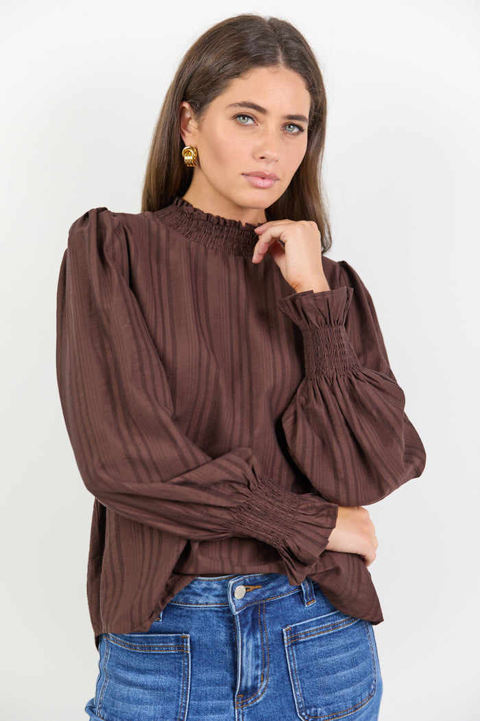 Woman wearing a brown blouse with puffed sleeves and blue jeans on a white background