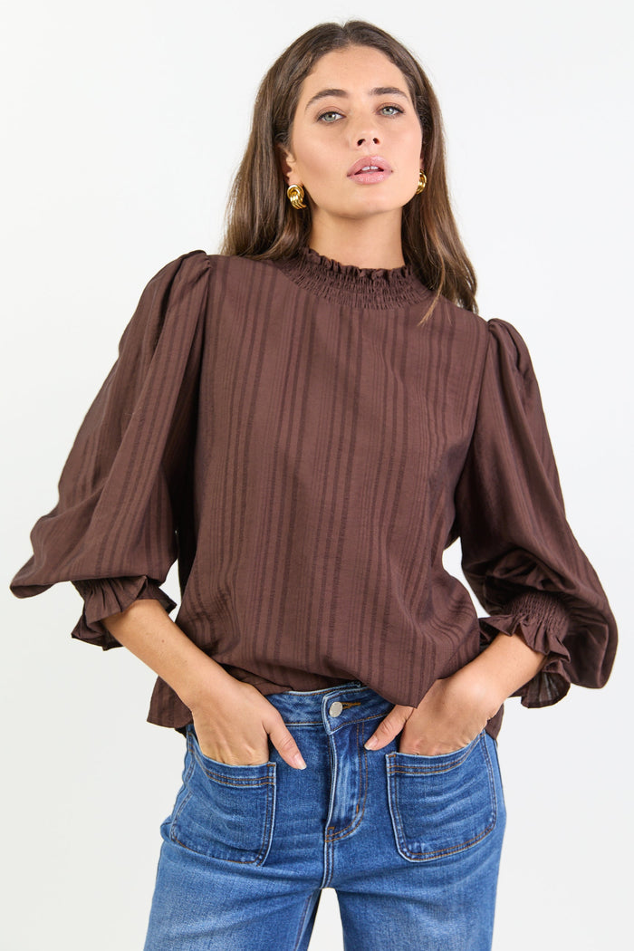Woman wearing a brown blouse with puffed sleeves and blue jeans on a white background