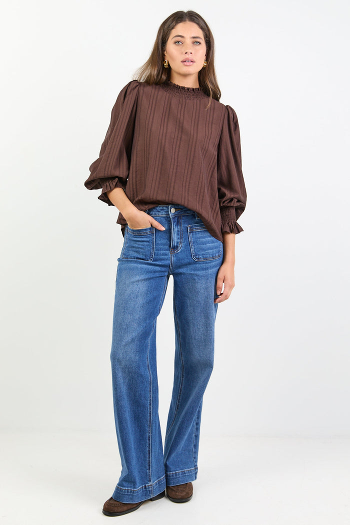 Woman wearing a brown blouse and blue jeans on a white background