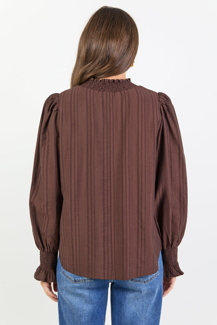 Woman wearing a brown blouse with puffed sleeves and blue jeans on a white background