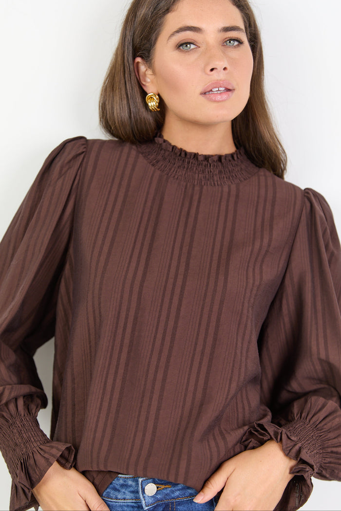 Woman wearing a brown pleated blouse against a white background