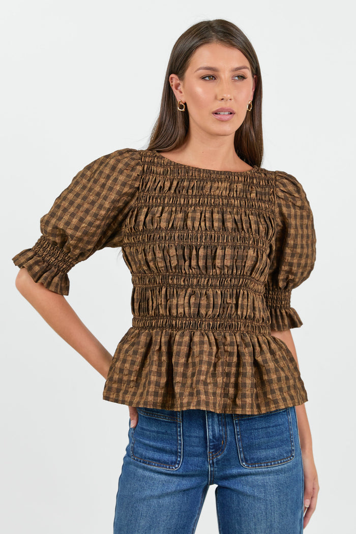 A woman wearing a chocolate and caramel checkered smocked top with puffed short sleeves, paired with high-waisted blue jeans.
col_pattern