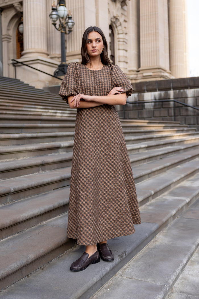 Woman in a patterned dress standing on stone steps in front of a classical building.