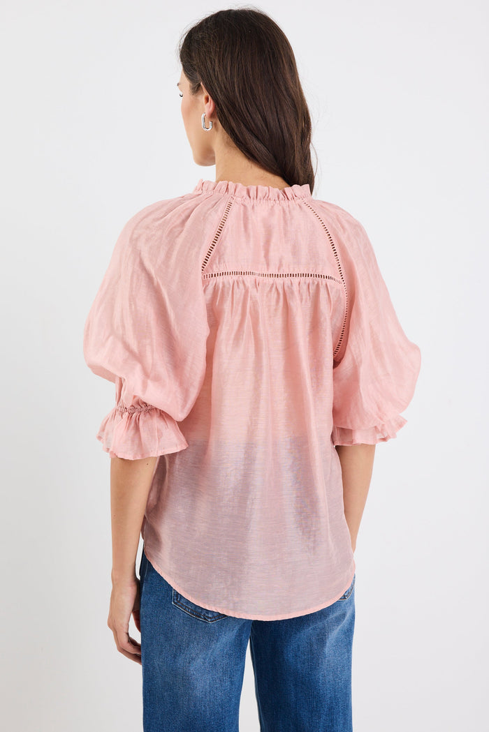 Woman wearing a pink blouse with ruffled sleeves on a white background