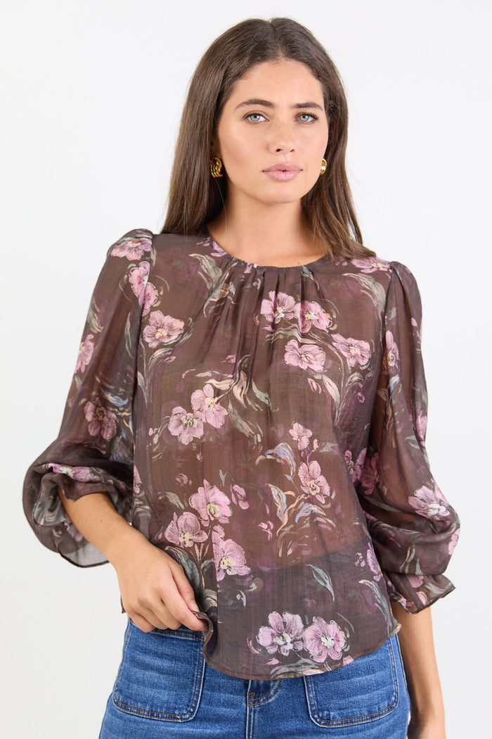 Woman wearing a floral blouse with sheer sleeves on a white background