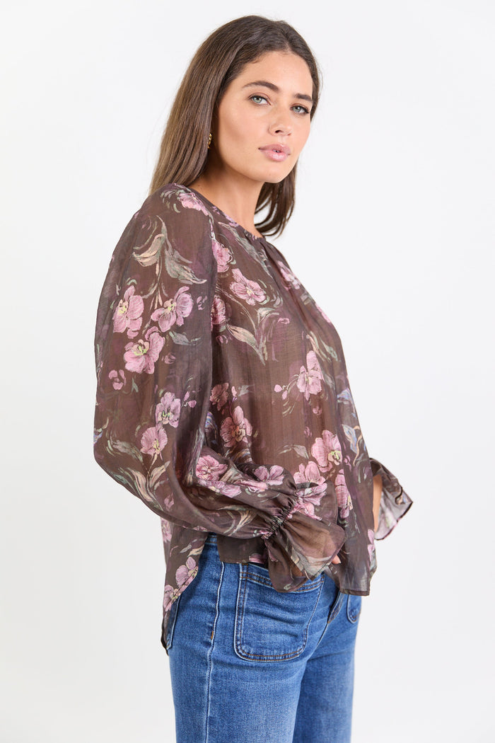Woman wearing a floral blouse with long sleeves and blue jeans on a white background