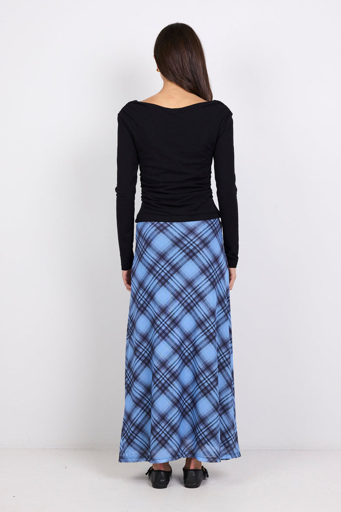 Person wearing a black long-sleeve top and blue plaid skirt on a white background