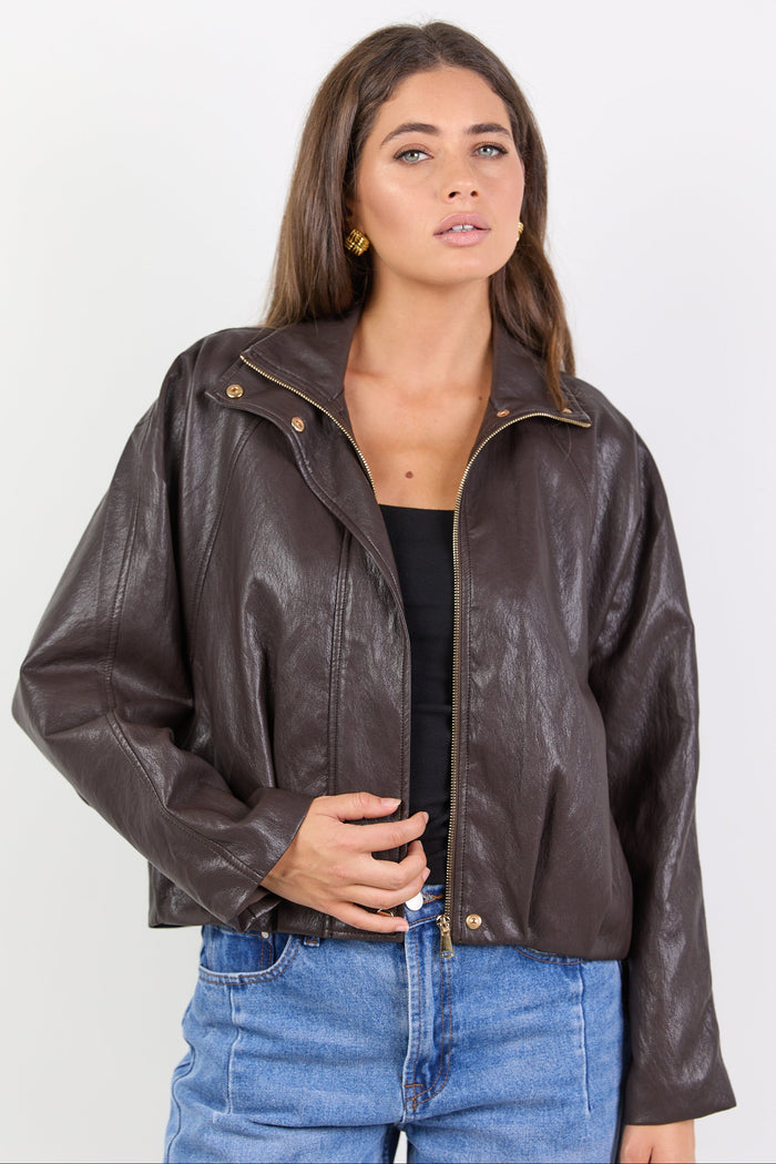 Woman wearing a brown leather jacket and blue jeans on a white background