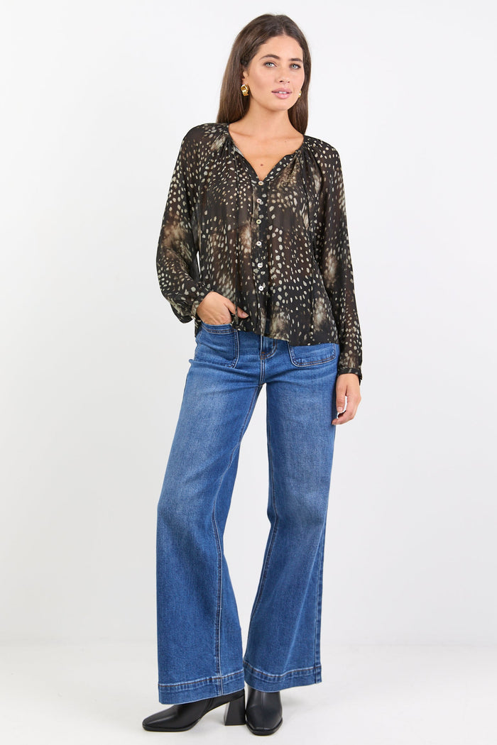 Woman wearing a black patterned blouse and blue jeans on a white background