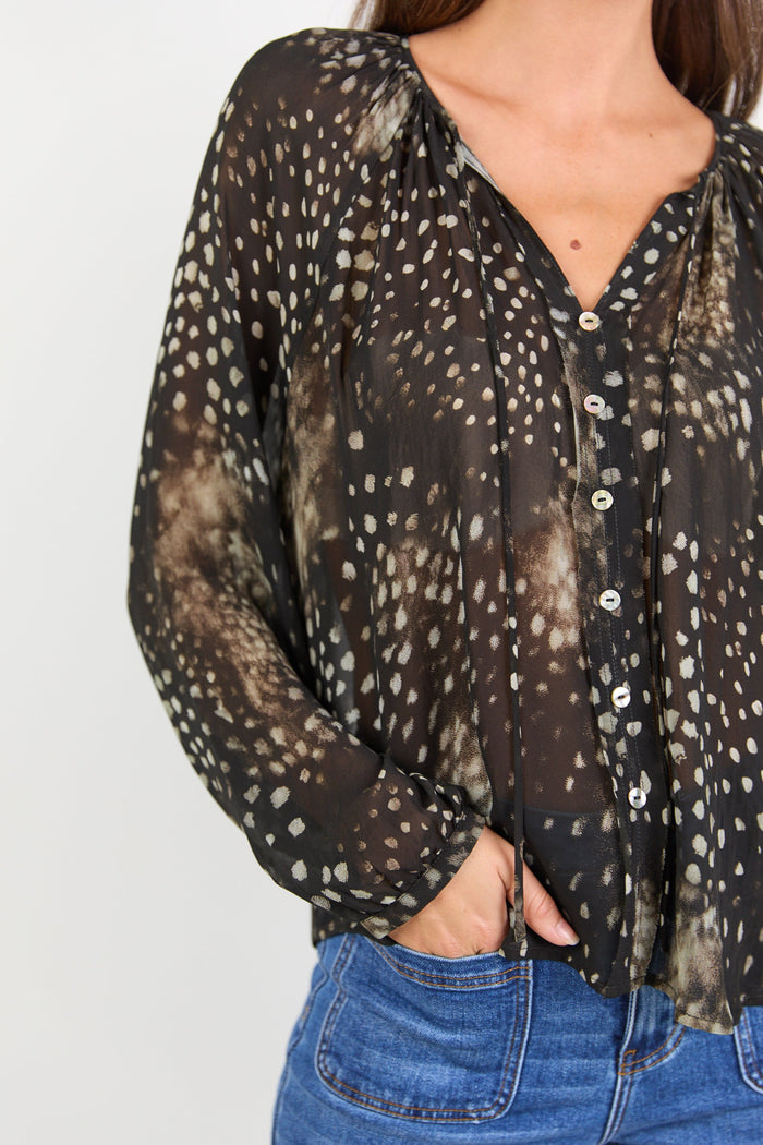 Sheer blouse with print and blue jeans on a plain background