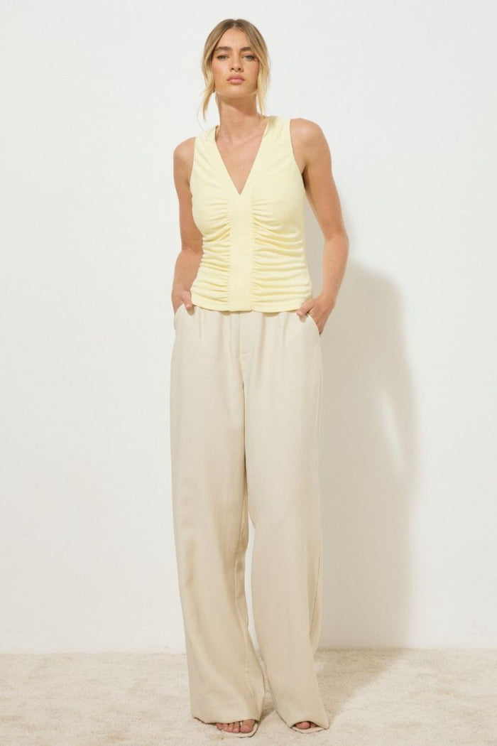 Lemon yellow sleeveless tank top with ruched bodice and centre band detail, styled with light beige wide-leg pants, worn by a model standing against a neutral background.
