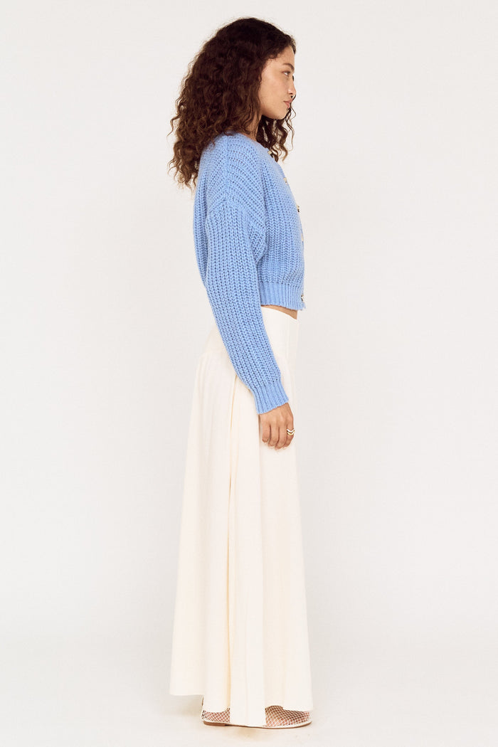Woman wearing a light blue sweater and white pants on a white background