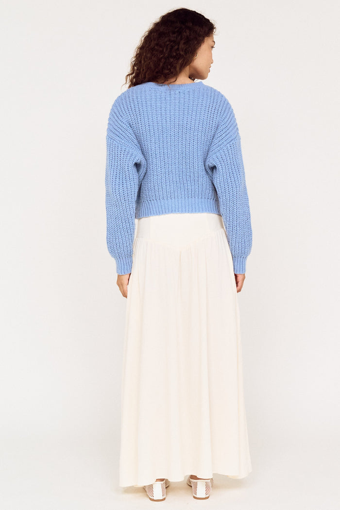 Person wearing a blue sweater and white skirt on a white background