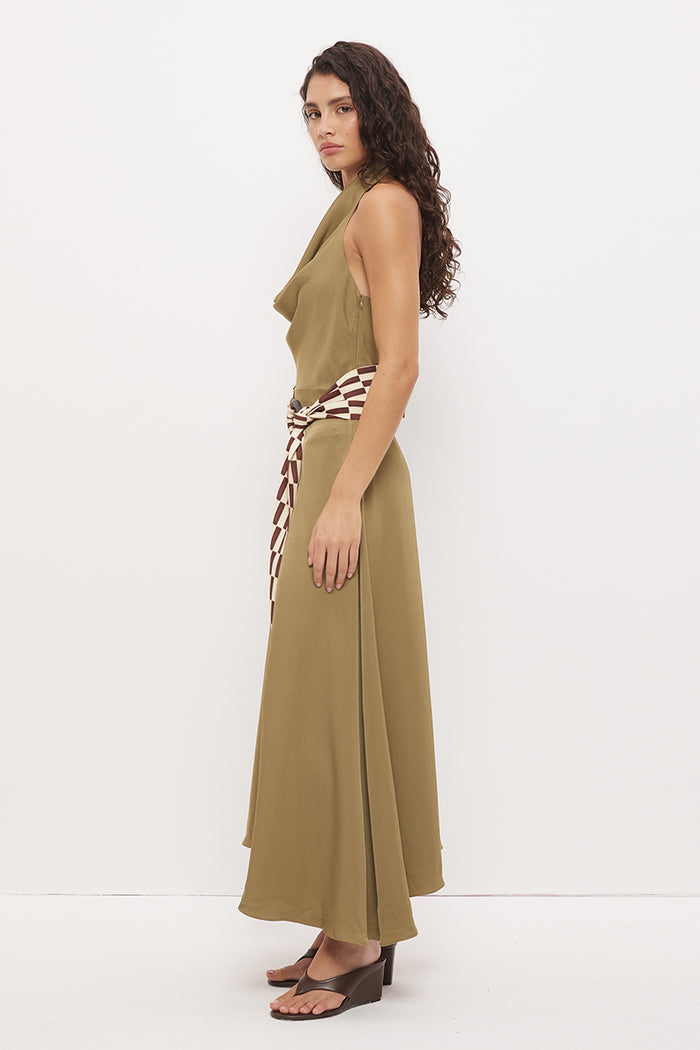A woman modeling a sleeveless olive green maxi dress with a brown and white patterned tie belt, shown from a side profile against a plain white studio background.