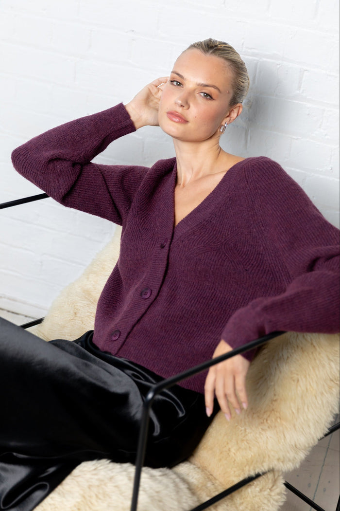 Woman wearing a purple cardigan sitting on a white bench.