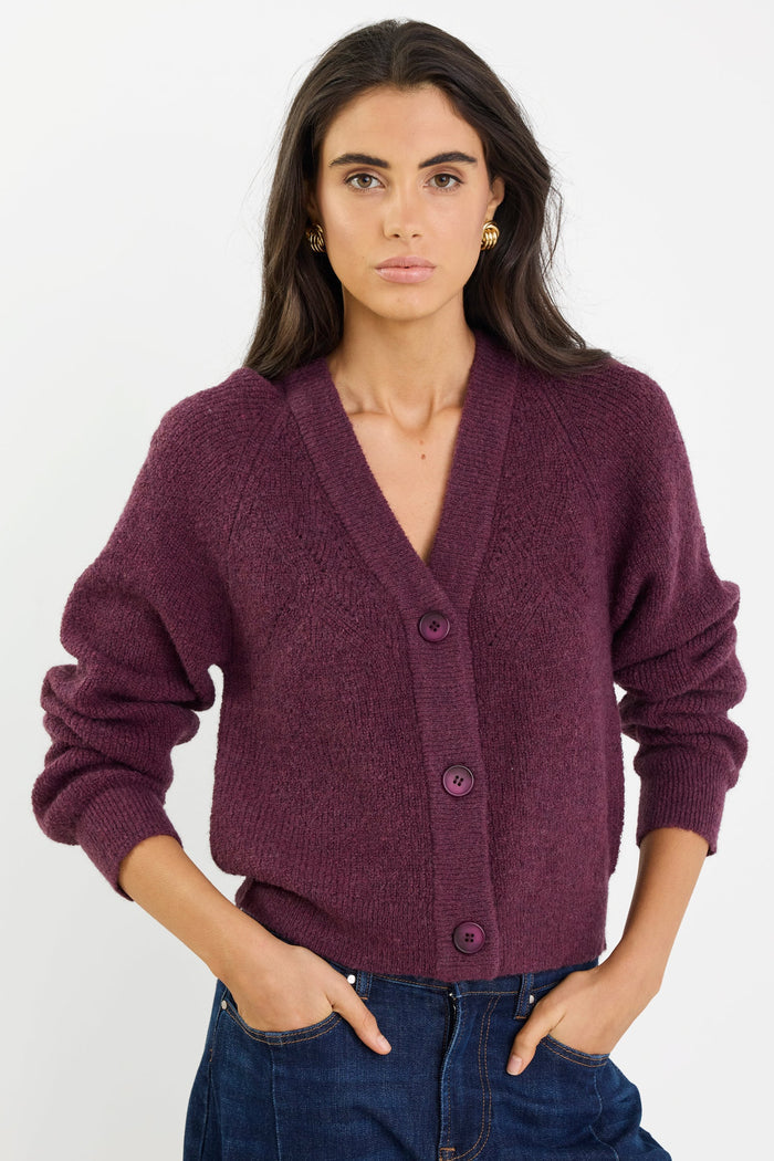 Woman wearing a purple cardigan and blue jeans on a white background