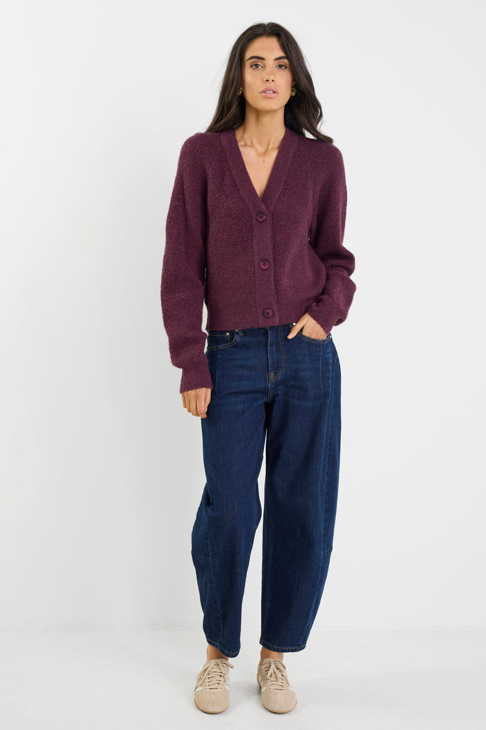 Woman wearing a purple cardigan and blue jeans on a white background