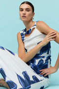 Woman wearing a sleeveless white midi dress with large blue floral print, featuring a side cutout detail and slim fit through the waist.