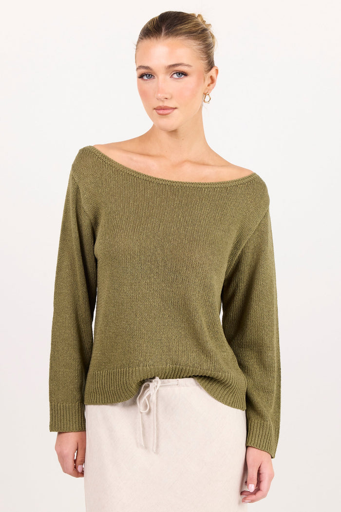 A woman modeling an olive green off-the-shoulder knit sweater with long sleeves, paired with a cream drawstring skirt, against a plain white studio background.