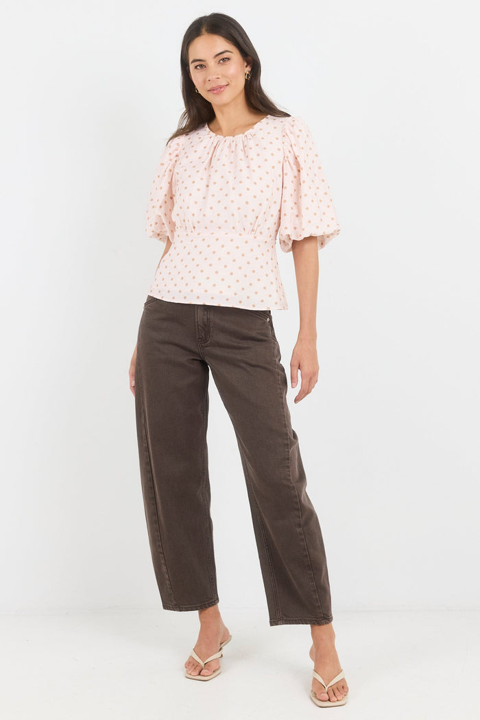 Woman wearing a patterned blouse and brown pants on a white background