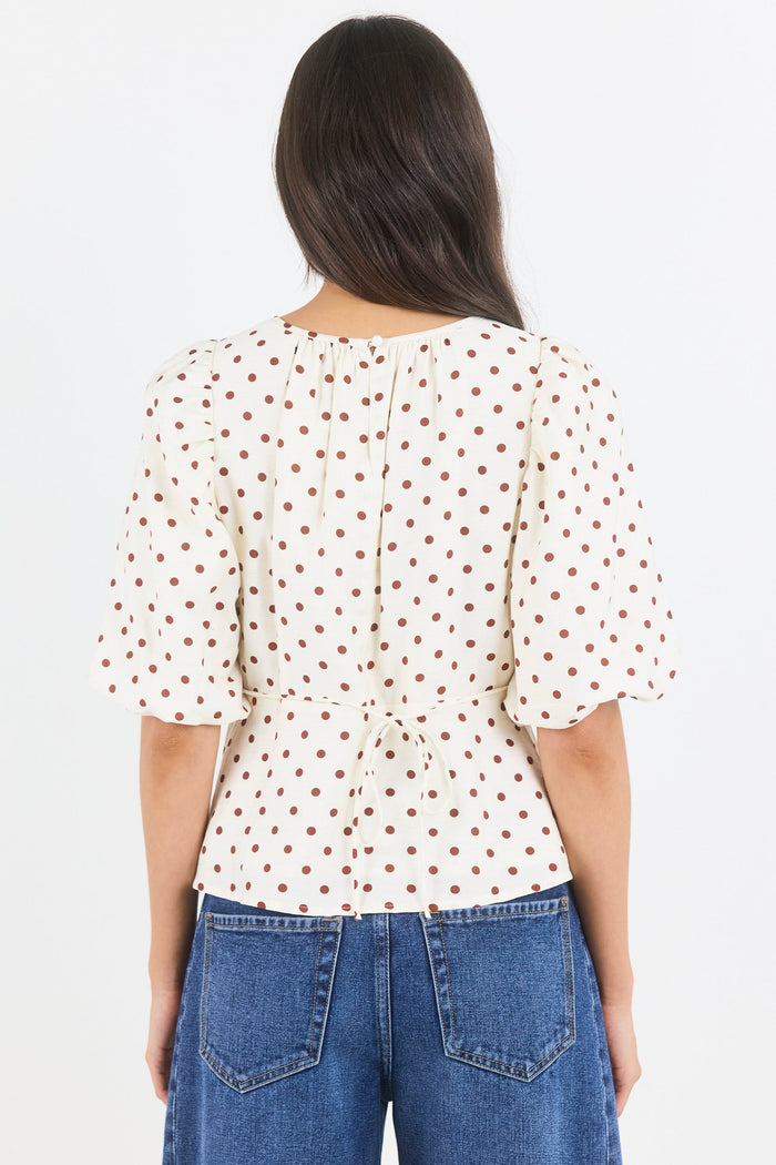 Person wearing a white blouse with red patterns and blue jeans on a light gray background