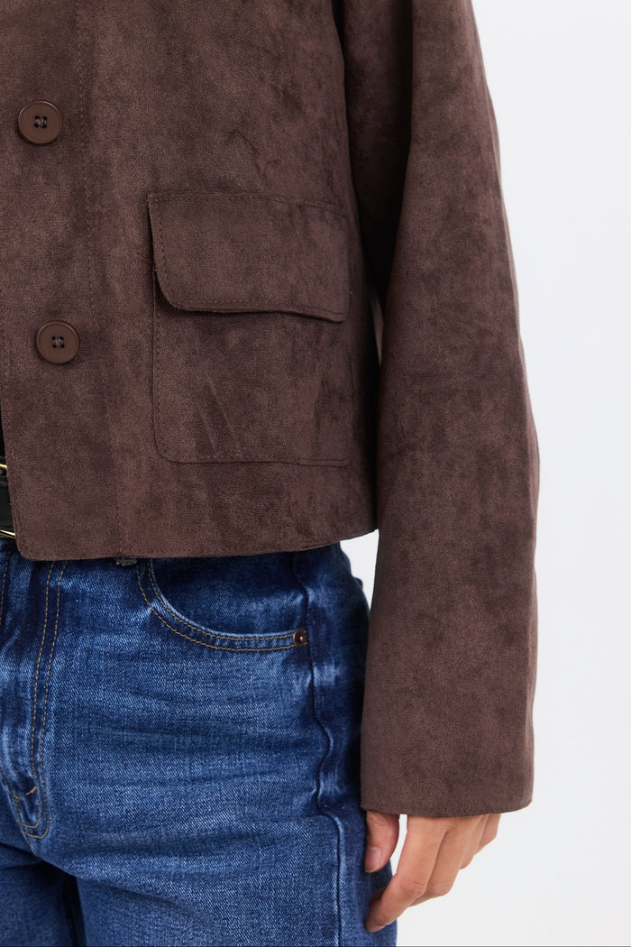 Brown suede jacket worn over a black shirt and blue jeans on a white background