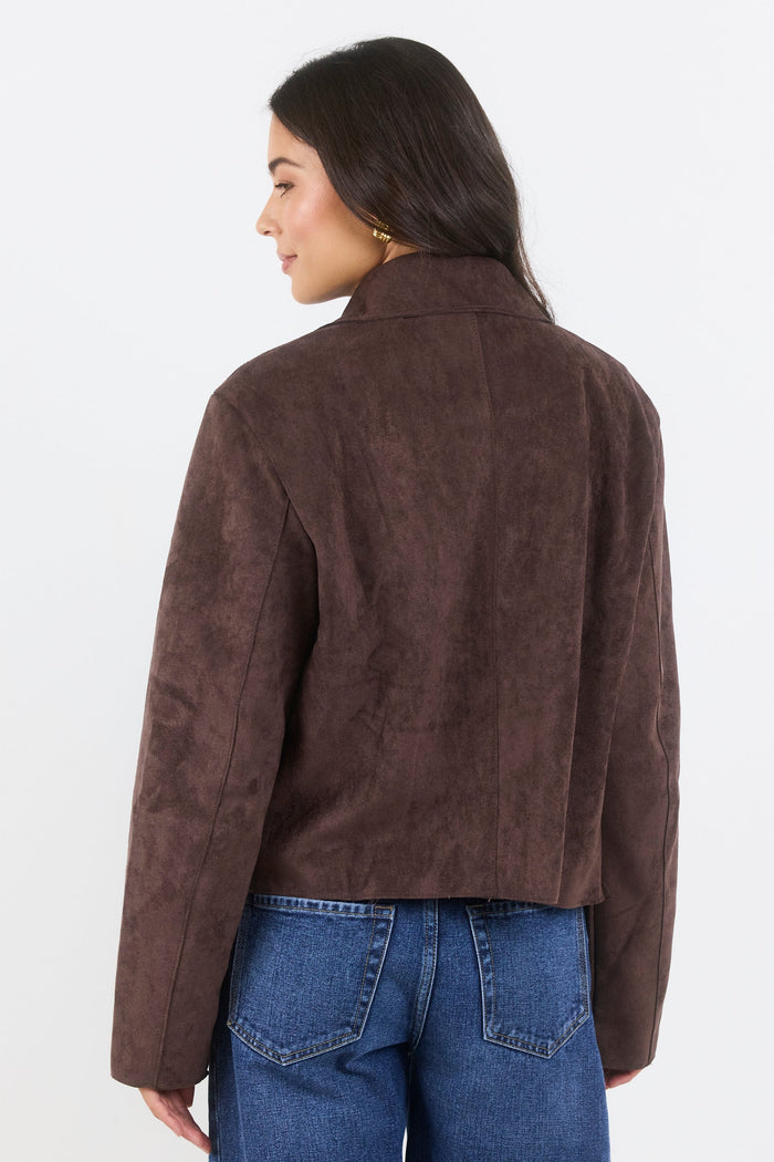 Person wearing a brown suede jacket and blue jeans on a white background