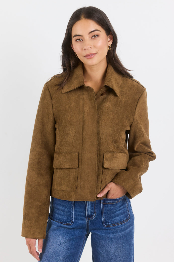 Woman wearing a brown suede jacket and blue jeans on a white background