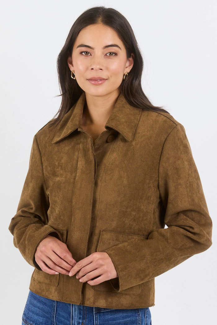 Woman wearing a brown suede jacket and blue jeans on a white background
