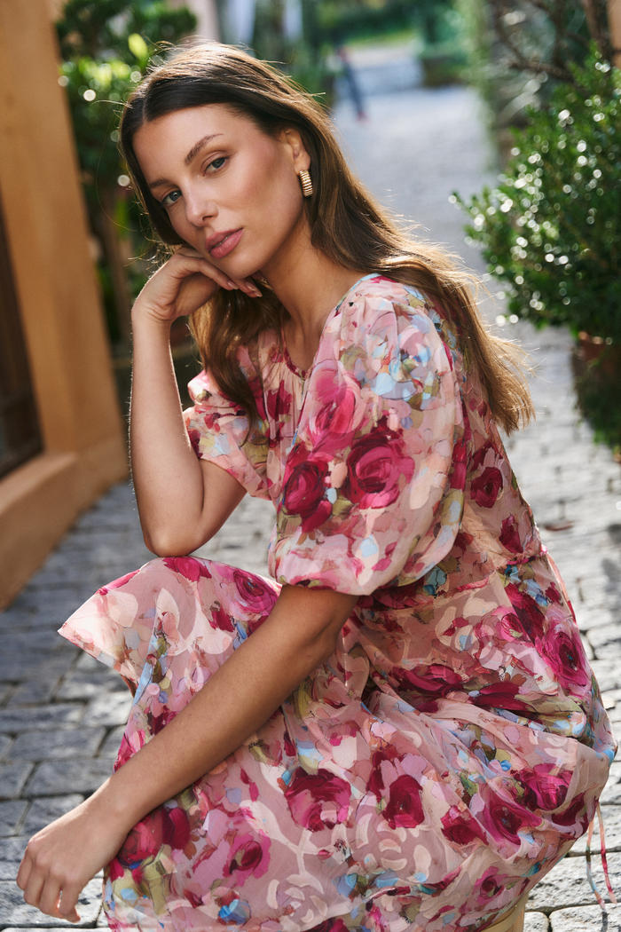Woman in a floral dress sitting outdoors on a stone path.