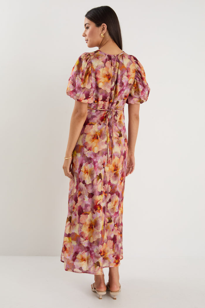Woman wearing a pink and multi-tone floral midi dress with puff short sleeves, bias cut, and lined finish.