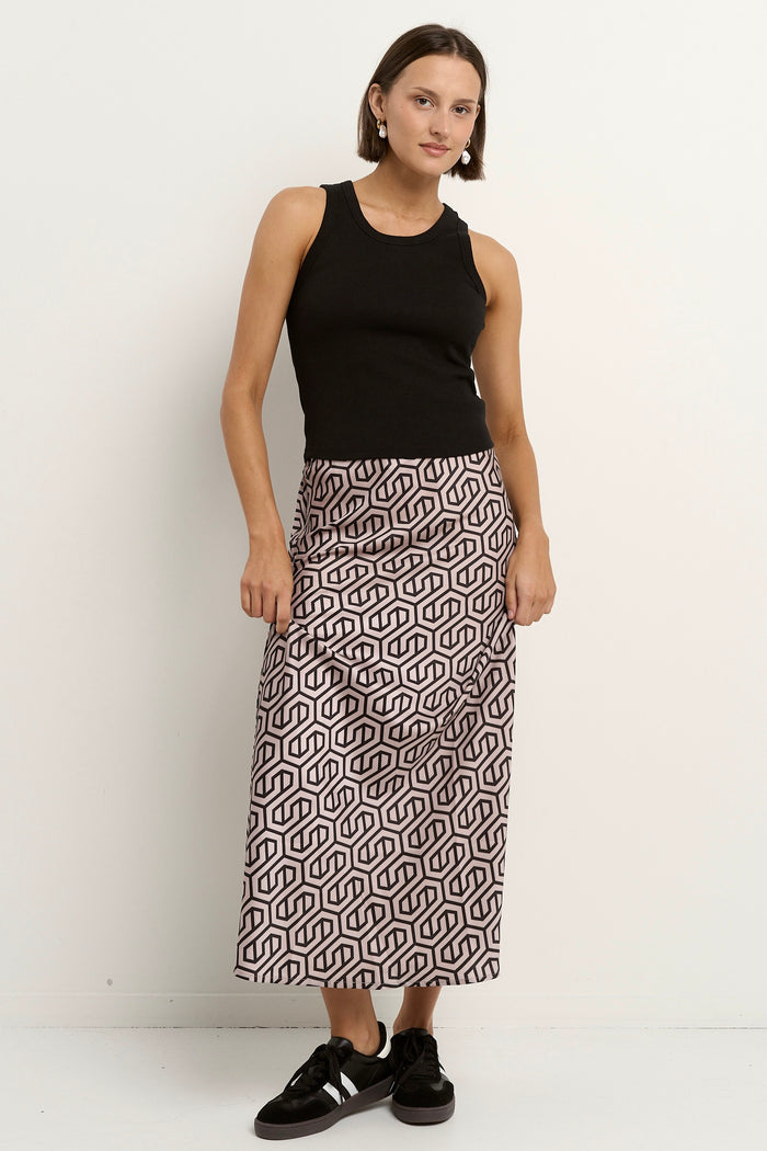Woman wearing a blush and black geometric print satin midi skirt with a black tank and sneakers.