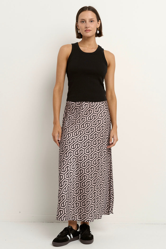 Woman wearing a blush and black geometric print satin midi skirt with a black tank and sneakers.