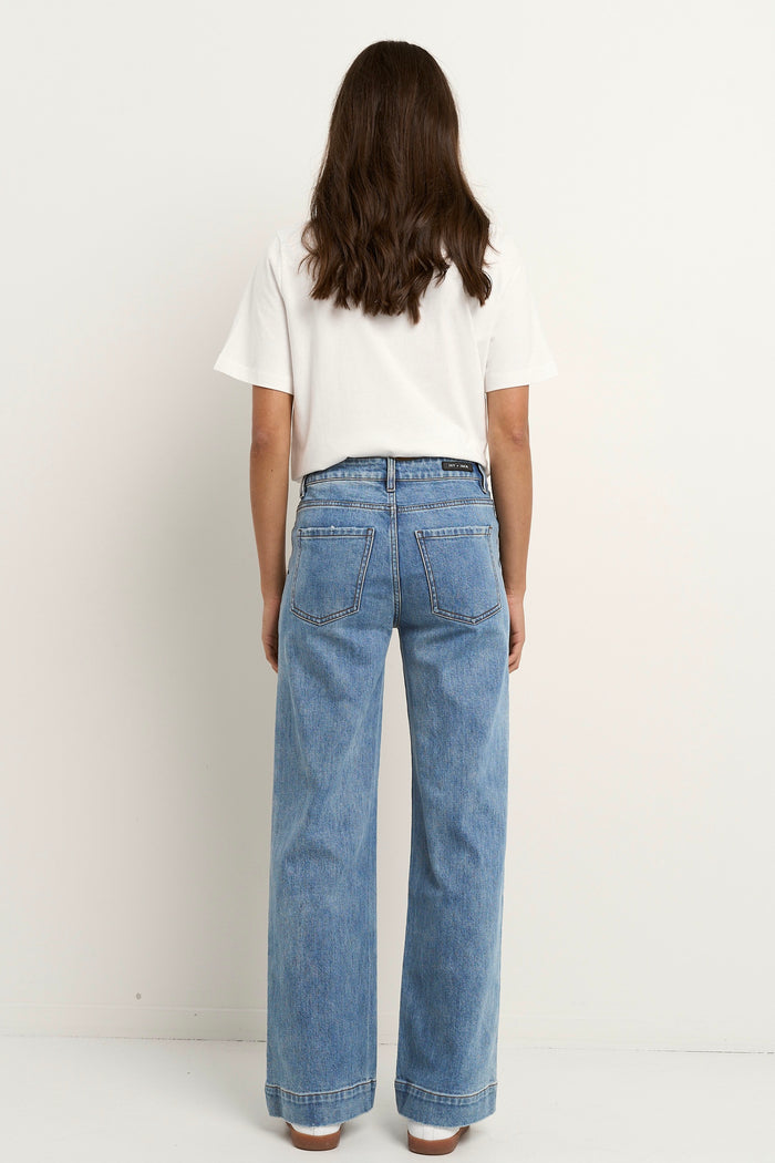 Woman wears a white tee with mid-rise, wide-leg blue jeans featuring front patch pockets and a relaxed silhouette.