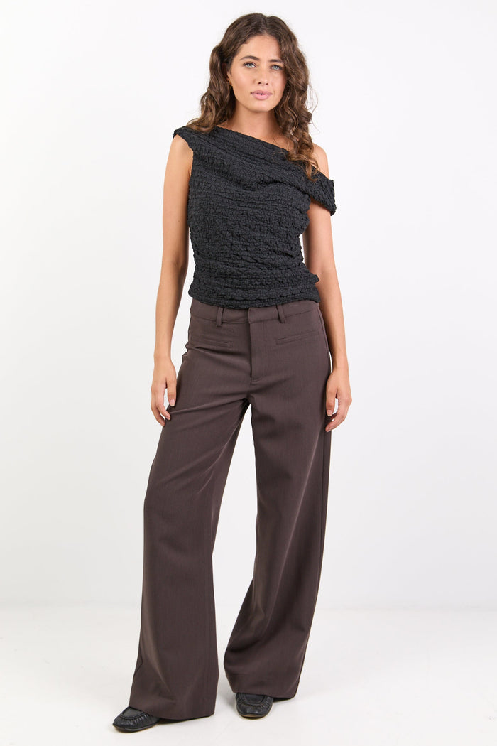 Woman wearing a black top and brown pants on a white background