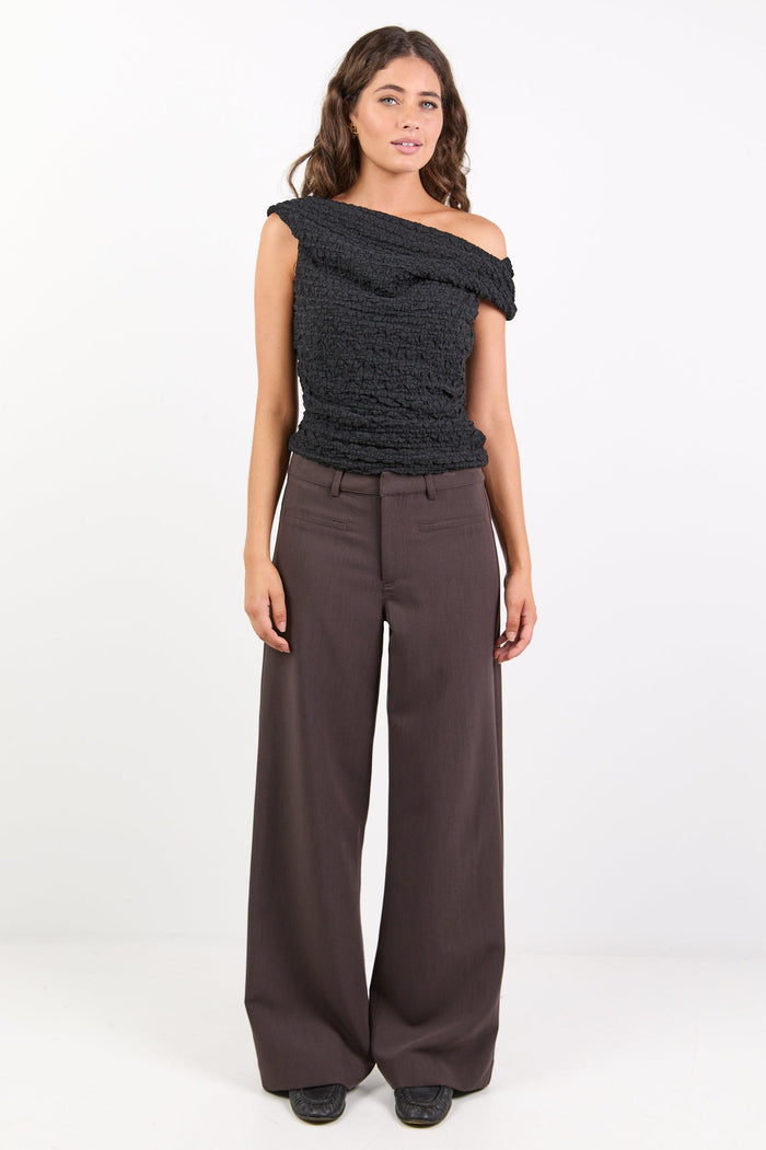 Woman wearing a black off-shoulder top and brown wide-leg pants on a white background