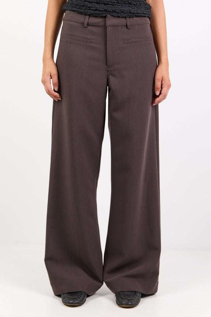 Person wearing a black textured top and brown wide-leg pants on a white background