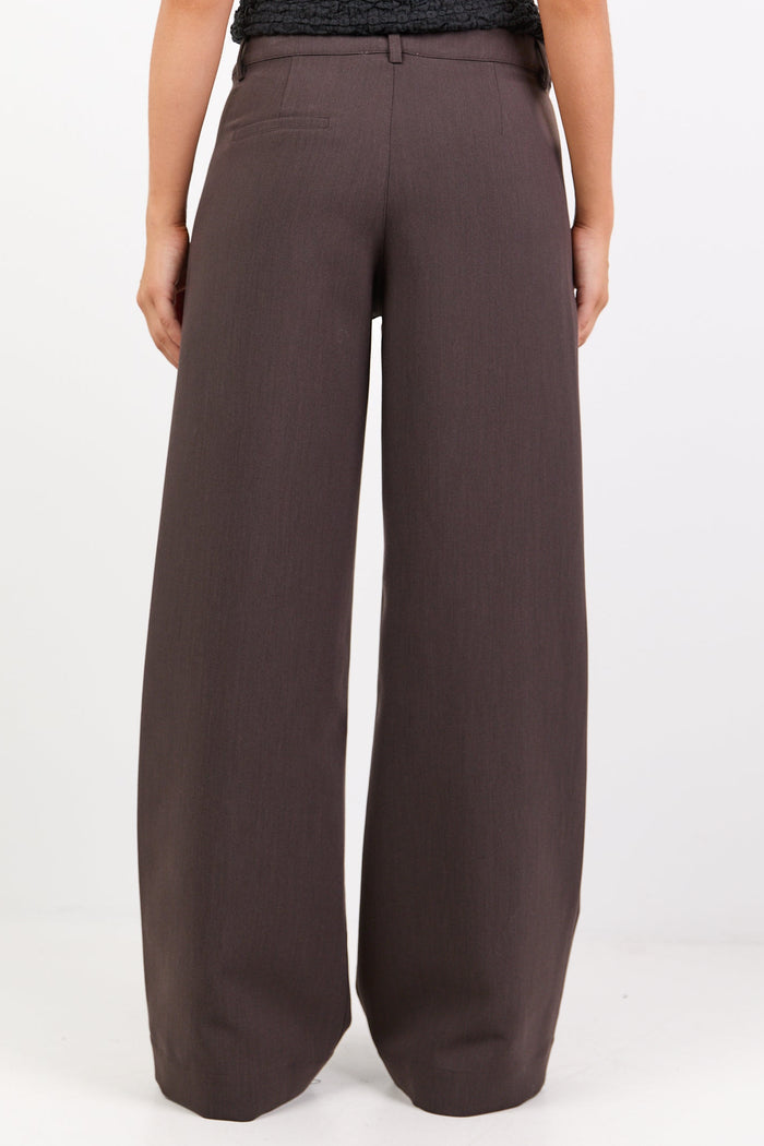 Woman wearing a black off-shoulder top and brown wide-leg pants on a white background
