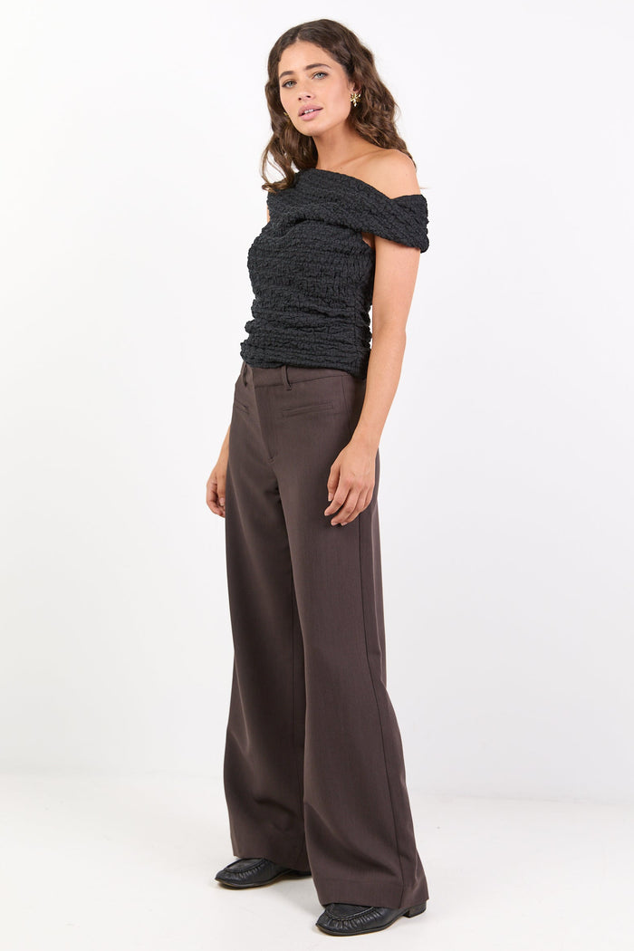 Woman wearing a black off-shoulder top and brown wide-leg pants on a white background