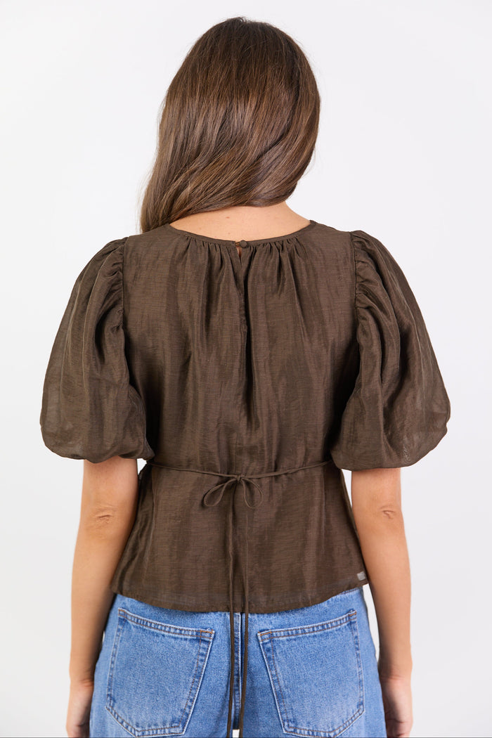 Woman wearing a brown blouse with puffed sleeves and blue jeans on a white background