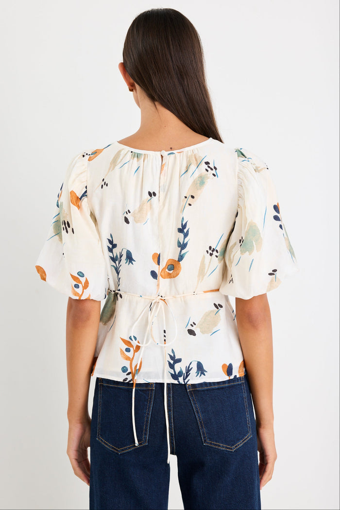 Woman wearing a cream and patterned top with blue jeans