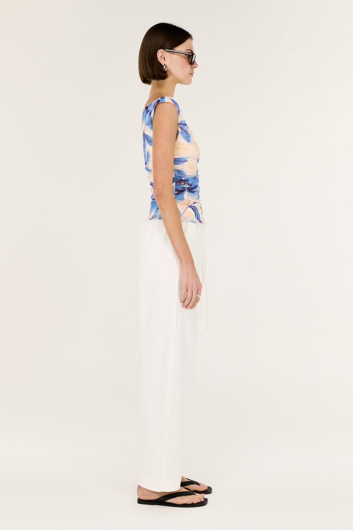 Woman wearing a blue and white patterned top with white pants on a plain background