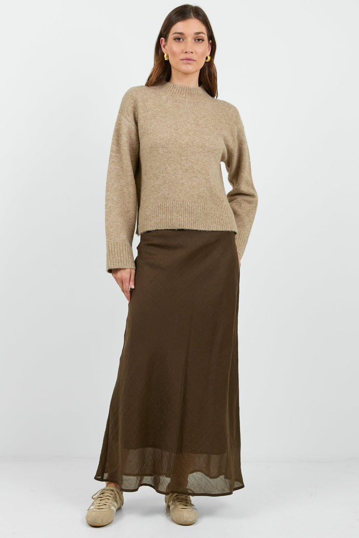 Woman wearing a beige sweater and brown skirt on a white background