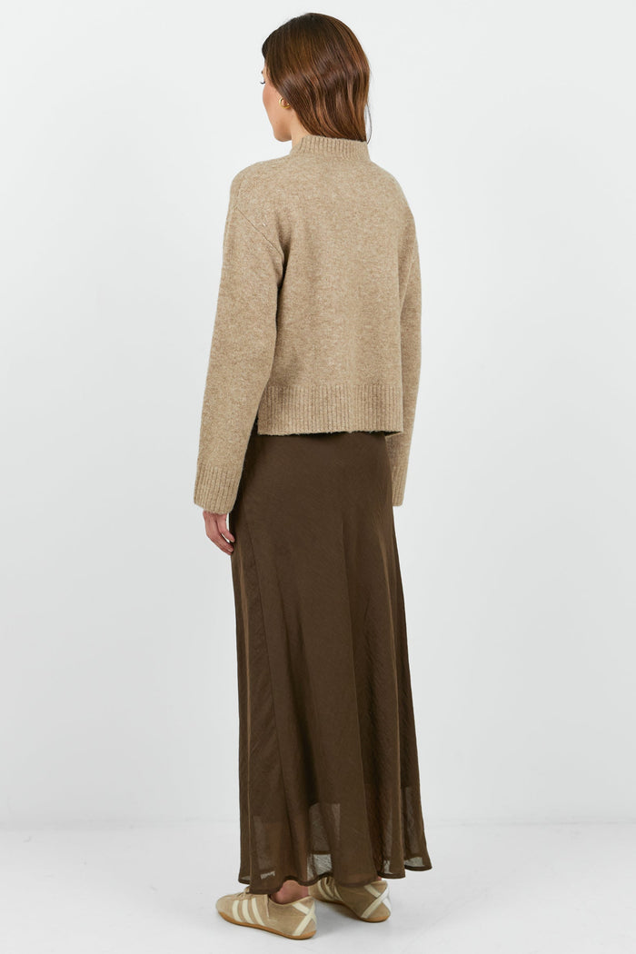 Person wearing a beige jacket and brown skirt on a white background