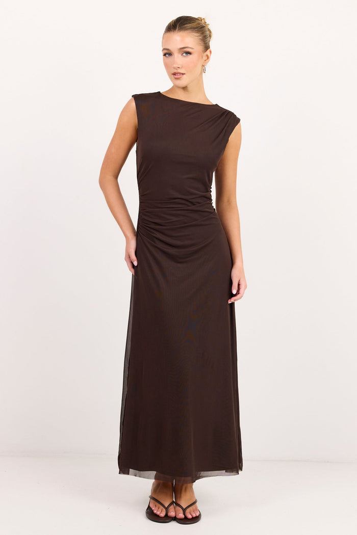 A woman modeling a sleeveless, dark brown maxi dress with a draped, gathered waist, standing against a plain white studio background.