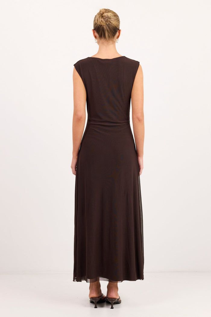 A woman viewed from behind wearing a sleeveless dark brown maxi dress with a gathered waist, standing against a plain white studio background.